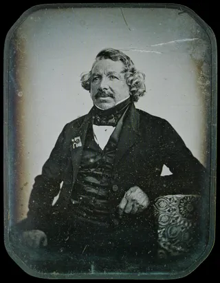 A black-and-white portrait of an older man seated, wearing a dark jacket and cravat, looking slightly to the side. The image shows the soft, slightly blurred texture typical of early daguerreotypes.