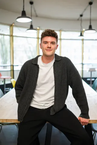 Bild von BRYGHT-Gründer Til Wiesenberg in einem Büroraum. Til sitzt angelehnt an einem Tisch und lächelt in die Kamera.