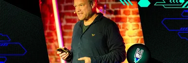 Sebastian Deutsch bei seinem Vortrag auf dem DMKR, während er über „Transformational AI“ spricht; er steht vor einer beleuchteten Backsteinwand, spricht engagiert ins Publikum und hält ein Smartphone in der Hand.