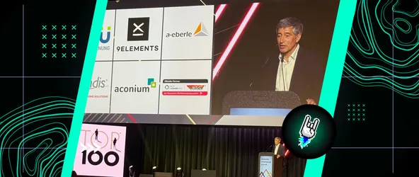 Ranga Yogeshwar auf der Bühne der Top 100-Preisverleihung, im Hintergrund eine Leinwand der Preisträger mit unter anderem dem Logo von 9elements.